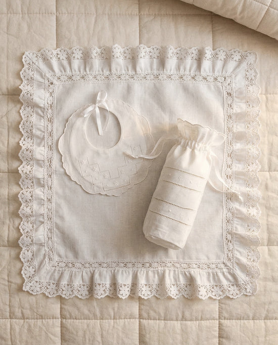 Set babero y porta biberón de lino bordado flor sobre cama y arrullo