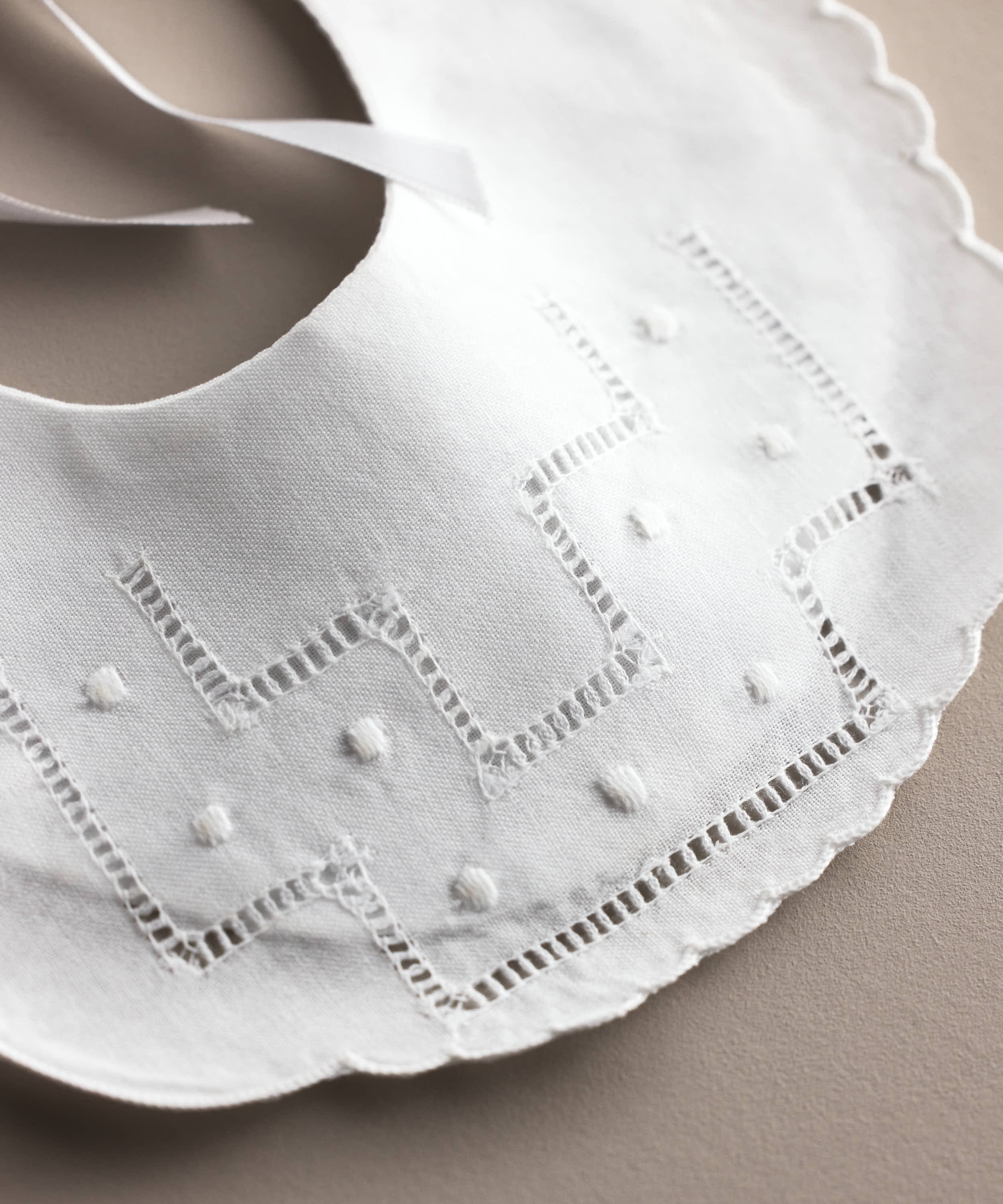 Detalle de la vainica y los bodoques bordados del babero de bebé de lino blanco, confeccionado artesanalmente en España — Tinylace
