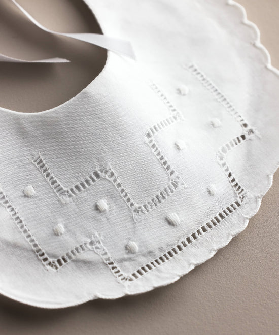 Detalle de la vainica y los bodoques bordados del babero de bebé de lino blanco, confeccionado artesanalmente en España — Tinylace
