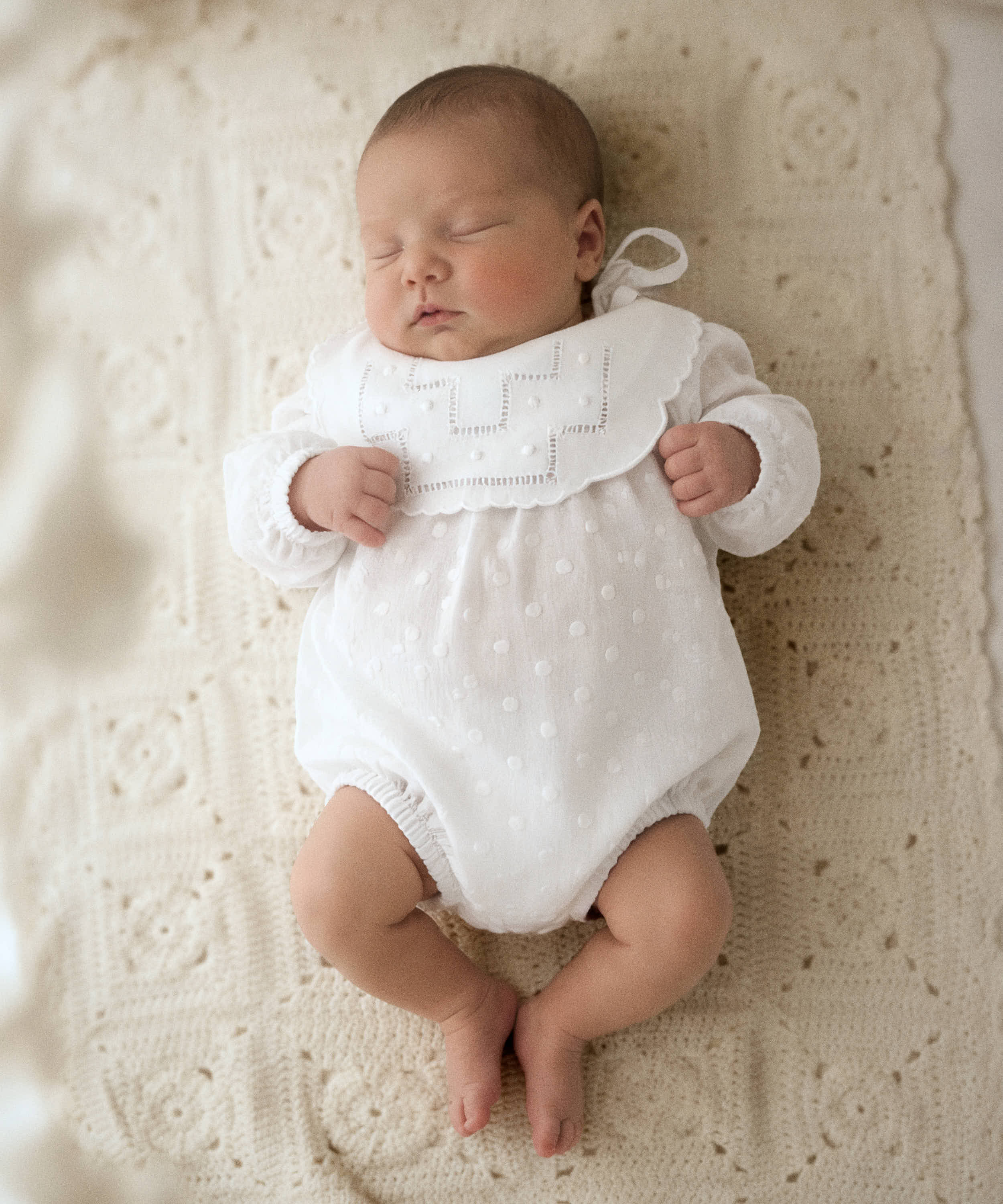 Recién nacido con babero de lino blanco con vainica y bodoques de Tinylace, ropa de bebé artesanal hecha en España