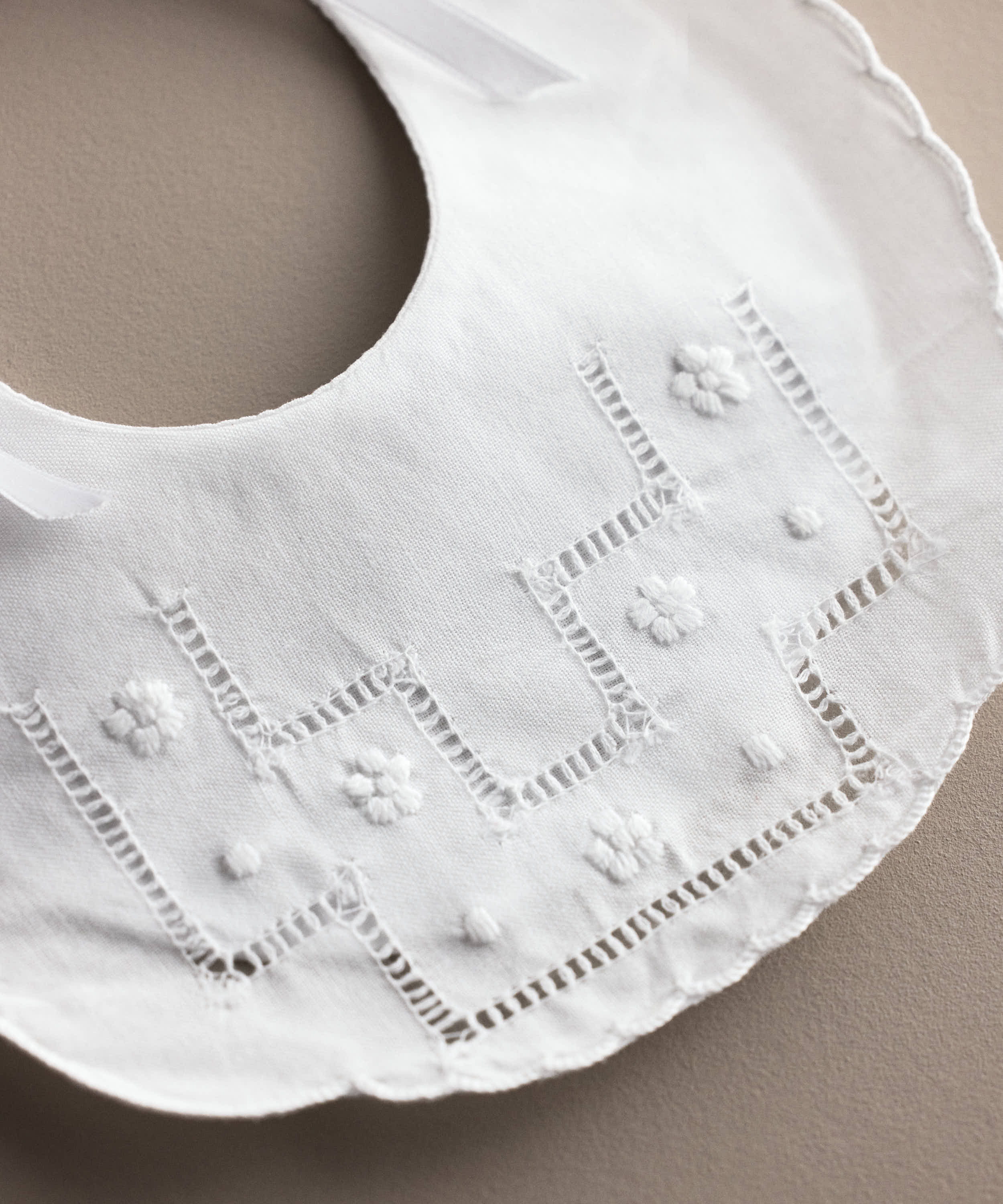 Detalle de la vainica y las flores bordadas del babero de bebé de lino blanco, confeccionado artesanalmente en España — Tinylace
