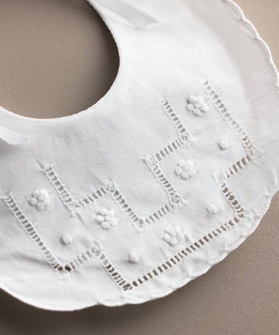 Detalle de la vainica y las flores bordadas del babero de bebé de lino blanco, confeccionado artesanalmente en España — Tinylace