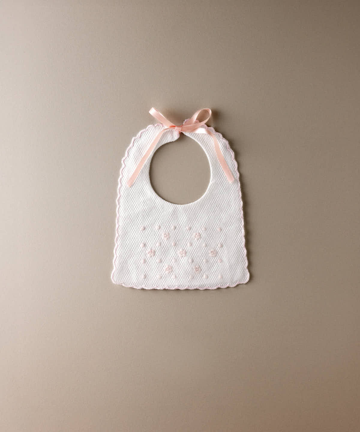 Babero de bebé de piqué blanco con flores y bodoques bordados en rosa y lazada de raso