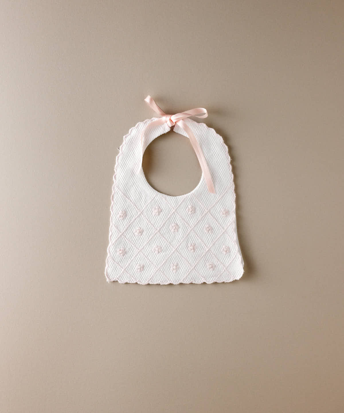 Babero de bebé de piqué blanco con flores bordadas en rosa en rombos y lazada de raso