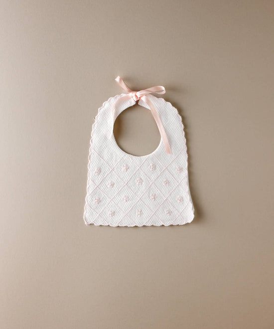 Babero de bebé de piqué blanco con flores bordadas en rosa en rombos y lazada de raso