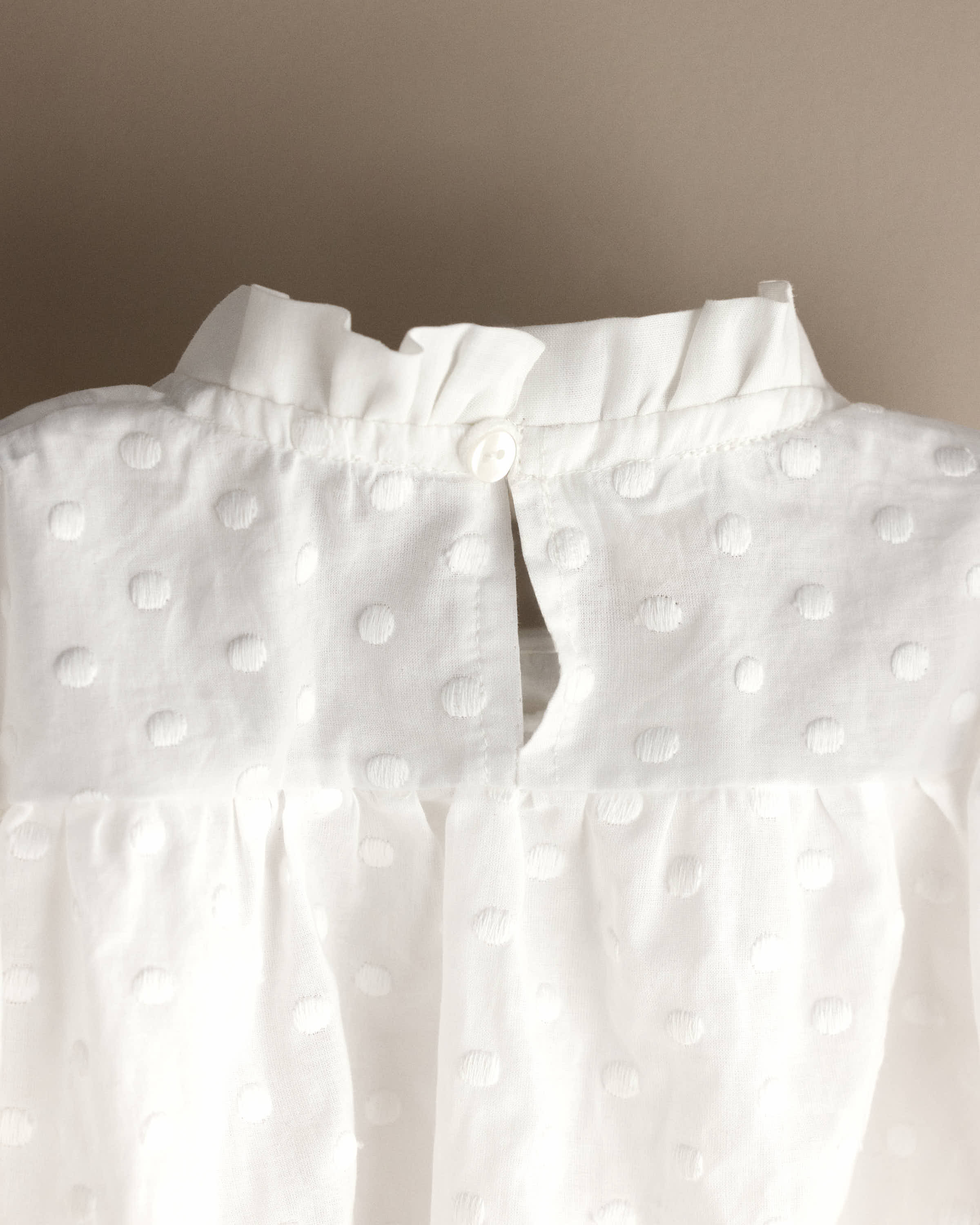 Detalle del cuello con volante y abertura trasera abotonada de un pelele de bebé de bodoques bordados  blanco, tejido de algodón bordado, moda infantil artesanal hecha en España — Tinylace