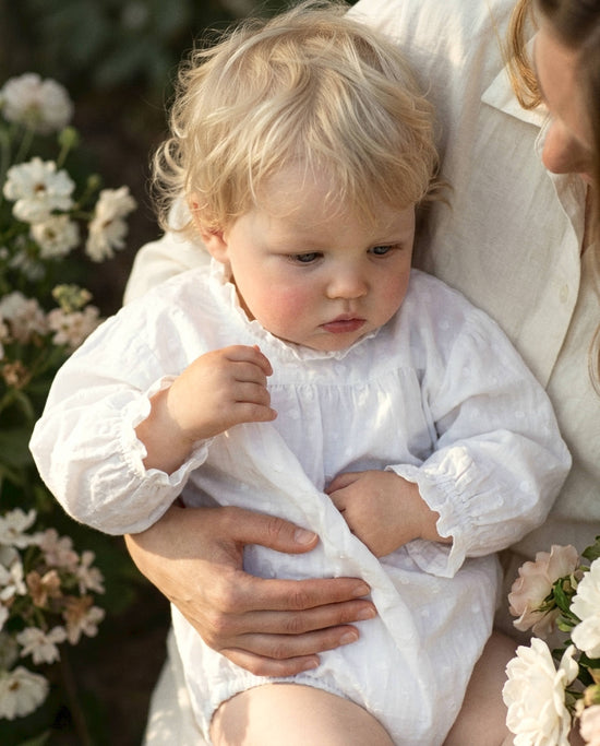 Bebé con pelele blanco algodón bordado bodoques entre flores — Tinylace